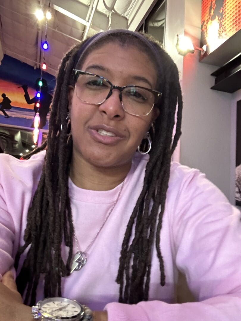 A woman with dreads and glasses is smiling.